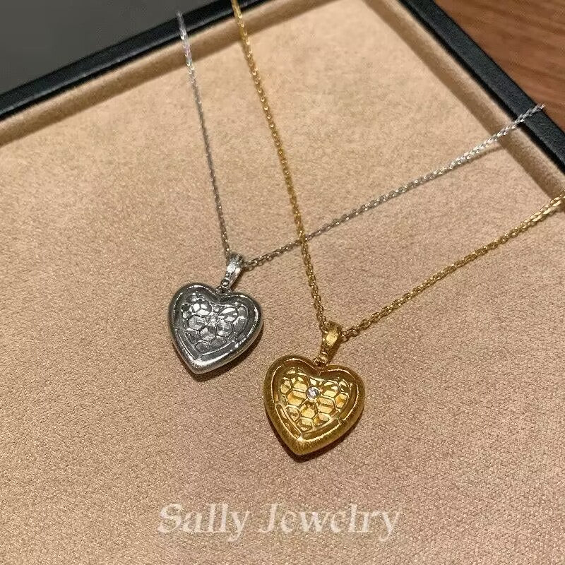 A close-up image of the Heart Brushed Necklace, featuring a heart-shaped pendant with a soft, matte finish. The pendant hangs from a delicate chain, creating a simple yet elegant design. The necklace is displayed against a neutral background, emphasizing its minimalist style and smooth texture.