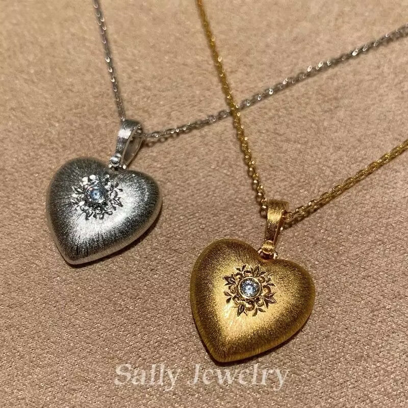 A close-up of the Heart Brushed Necklace featuring a heart-shaped pendant with a smooth, matte finish. The necklace is displayed against a neutral background, highlighting its sleek, minimalist design.