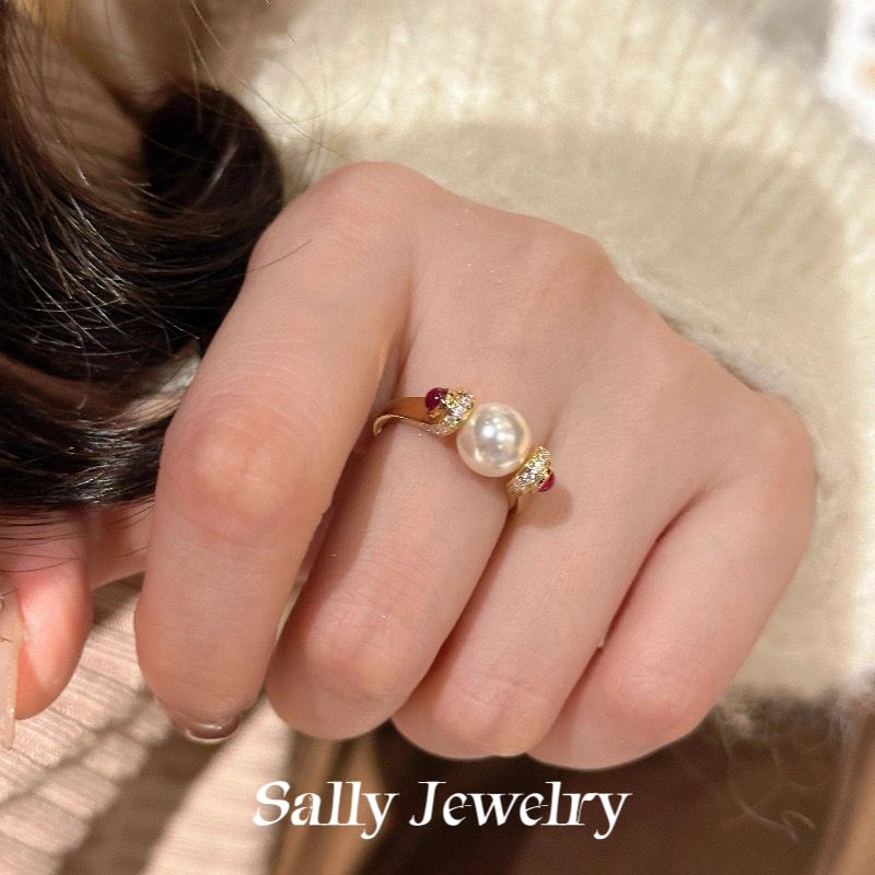  A close-up image of a model's hand wearing a stunning red corundum and pearl ring. The ring features a bright red corundum gemstone at its center, surrounded by lustrous pearls set in a sleek gold band. The hand is elegantly posed, highlighting the ring's intricate design and vibrant colors against a soft, neutral background.