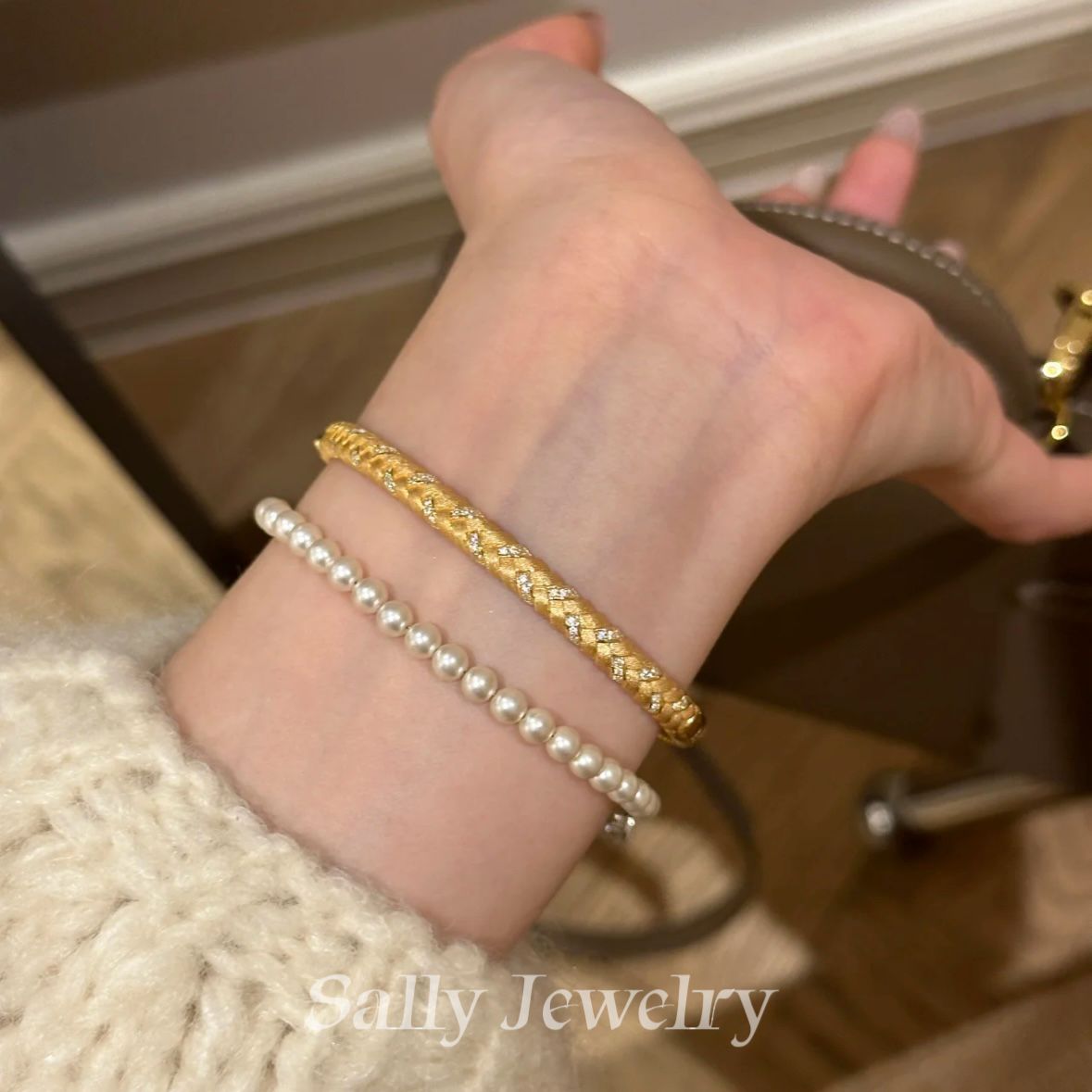 A close-up of the Wheat Brushed Bracelet in gold, worn on a model's wrist. The bracelet features a textured, brushed surface that evokes the elegance of wheat stalks, with the warm gold finish adding a luxurious and sophisticated touch to the model’s look.